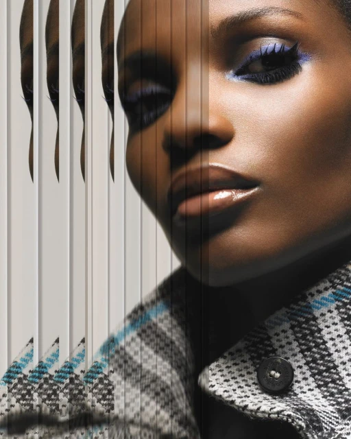 Close-up fashion shot of a black woman with blue eyeshadow, wearing a patterned coat, showcasing a modern editorial beauty aesthetic.