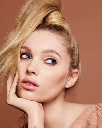 Close-up beauty portrait of a blonde woman resting her chin on her hand against a warm solid background