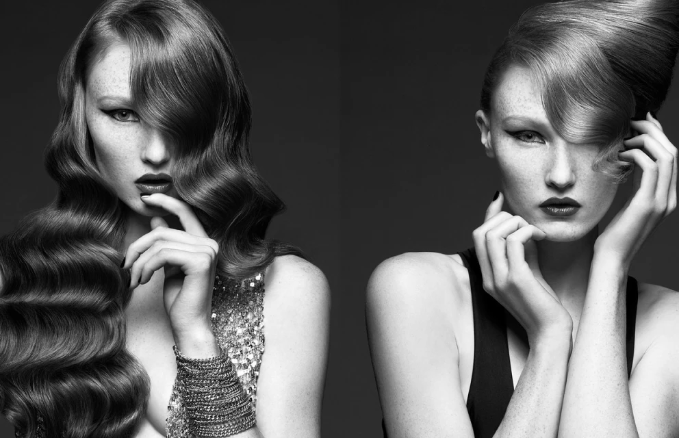 Monochrome portrait of two women with elegant hairstyles, dark lipstick, and minimal jewelry, set against a dark gray background.