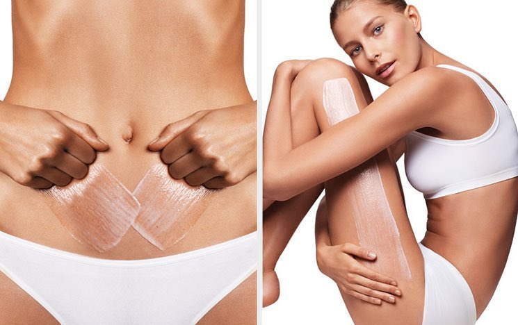 Studio shot of a fair-skinned young woman with an athletic build and bare midriff; product is being applied to her torso and legs.