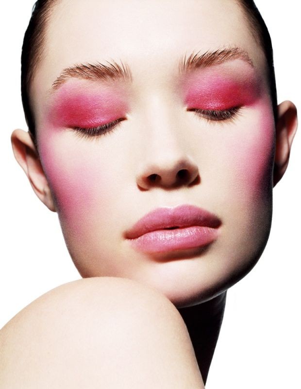 Close-up beauty portrait of a woman with vibrant pink eyeshadow and blush against a white background