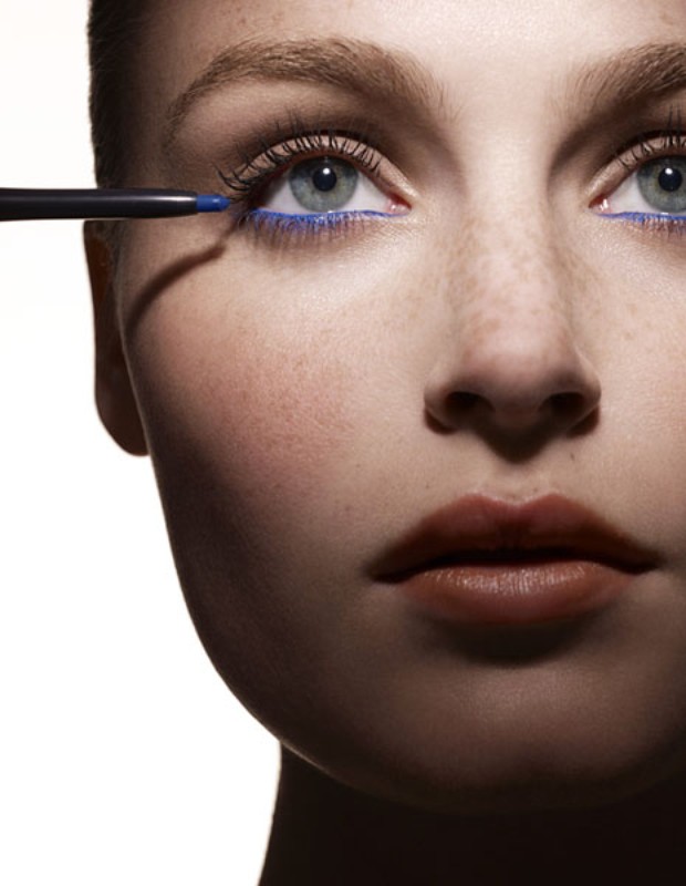 Close-up of a young woman's face, featuring blue eyeliner applied to her lower lash line with a black eyeliner pencil.