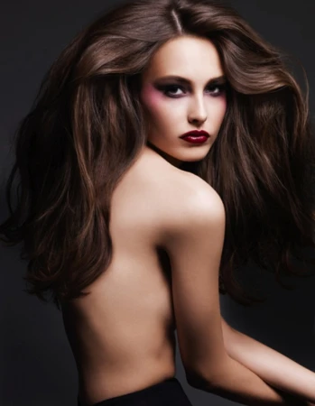 Portrait of a brunette woman with long hair styled in waves, dark eye makeup, and red lipstick against a dark gray backdrop.