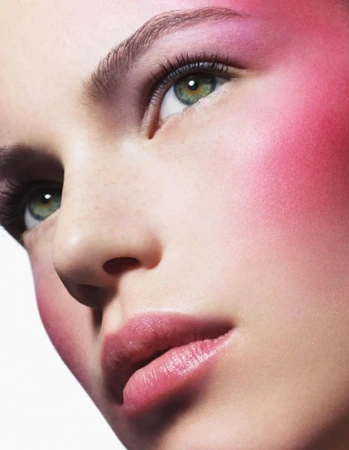 Close up beauty portrait of a woman with vibrant pink blush, dark mascara, and green eyes photographed by Philippe Salomon.