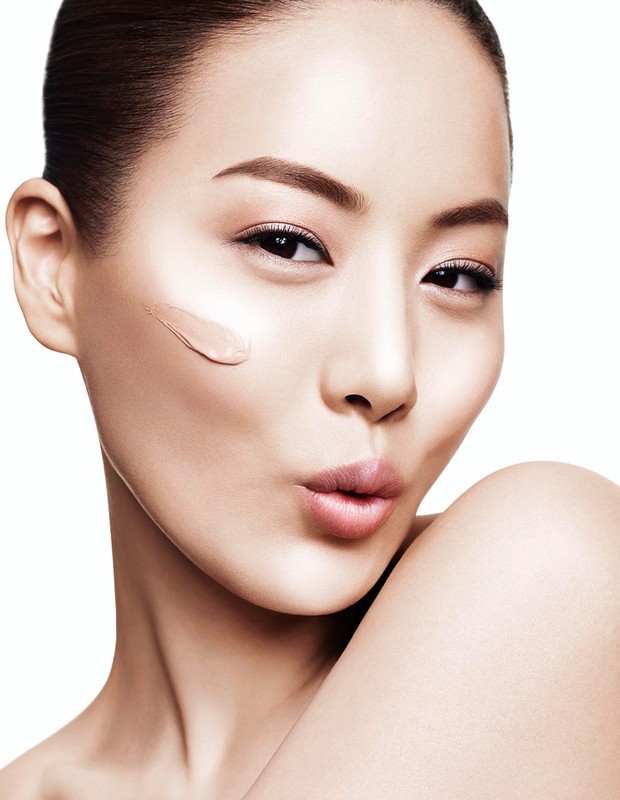 Close-up portrait of a woman with a smear of liquid foundation on her cheek, posing against a white background