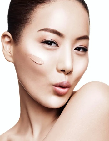 Close-up portrait of a woman with a smear of liquid foundation on her cheek, posing against a white background