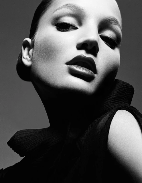 Striking black and white portrait of a woman with dramatic lighting highlighting her face and elegant black ruffled collar.