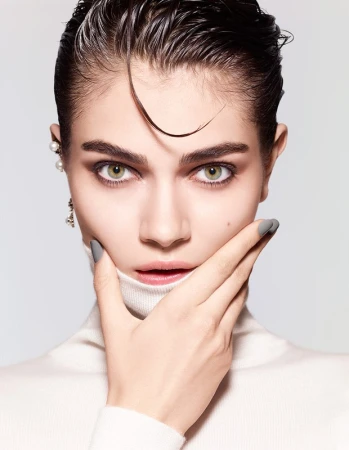 Close-up portrait of a woman with wet hair and grey nail polish holding hand to chin against a white background