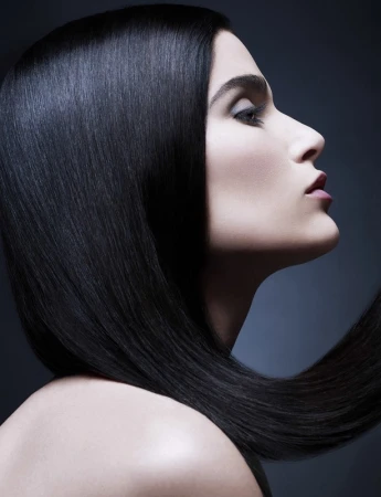 Profile portrait of a woman with long glossy black hair and soft makeup against a dark background by Philippe Salomon.
