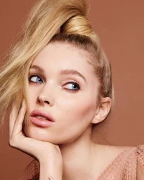 Close-up beauty portrait of a blonde woman resting her chin on her hand against a warm solid background