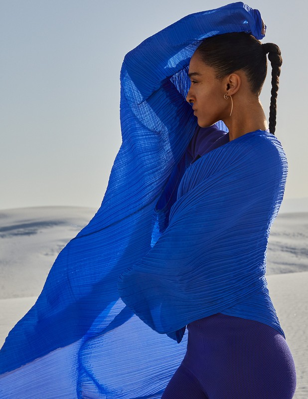 Woman in flowing blue top poses against a desert backdrop. The fabric billows around her as she looks to the side.