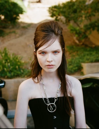 Portrait of a young woman with a 1960s beehive hairstyle, red graphic eyeliner, and layered silver chain necklaces wearing a black strapless top