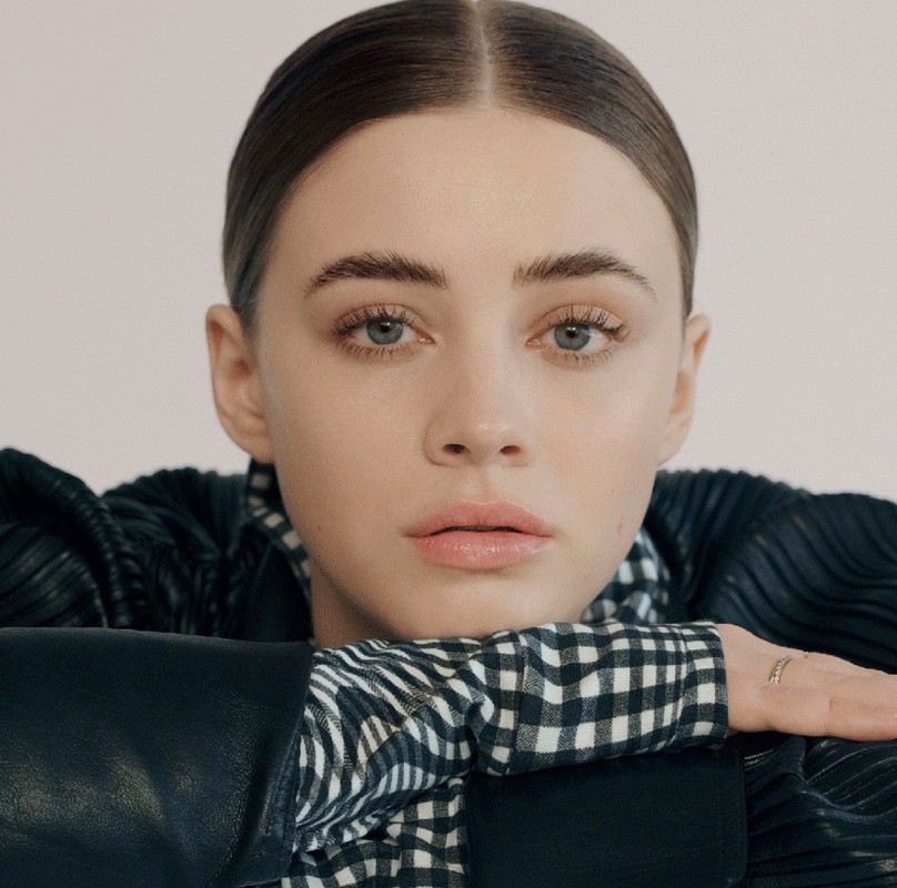 Close-up portrait of a woman resting her chin on her arms, wearing a black leather jacket and a black and white gingham shirt.