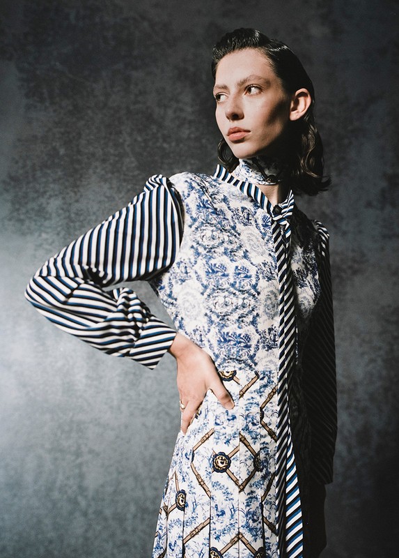 Model in patterned blue and white dress with striped sleeves posing against textured grey backdrop