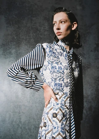 Model in patterned blue and white dress with striped sleeves posing against textured grey backdrop