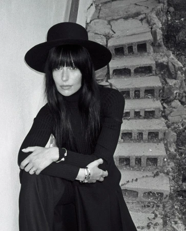 Monochrome portrait of a woman wearing a wide-brimmed black hat and turtleneck, seated on stone steps outdoors.