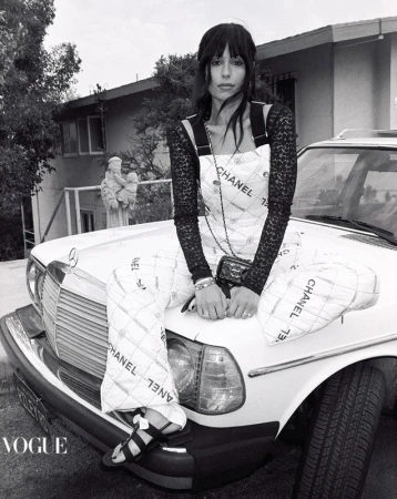 Black and white shot of a woman in a Chanel dress sitting on the hood of a classic car in front of a house and statue.