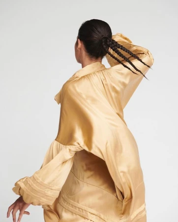 Model in a gold silk blouse with braided hair captured against a white background by Phoebe Seligman