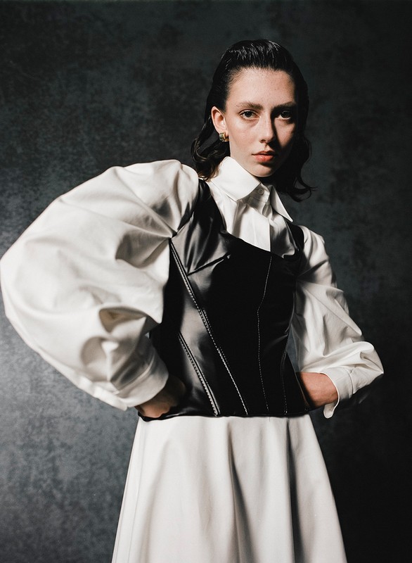 Woman in white shirt with voluminous sleeves and black leather corset posed against a textured grey background