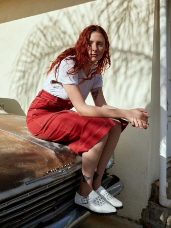 Red-haired woman sitting on the hood of a vintage car wearing a white t-shirt, red skirt, and white shoes