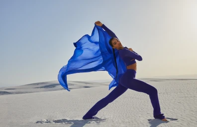 Woman in blue athletic wear posing with a vibrant blue flowing fabric in a vast sandy desert landscape