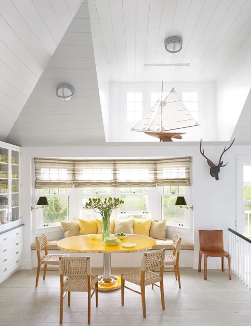 Bright and airy dining room features yellow table with woven chairs, and a sailboat decoration hanging near large windows.