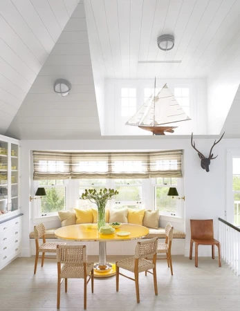 Bright and airy dining room features yellow table with woven chairs, and a sailboat decoration hanging near large windows.