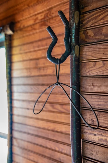 A decorative coat rack made of a wooden branch with an attached wire hanger, mounted on a wooden plank wall.