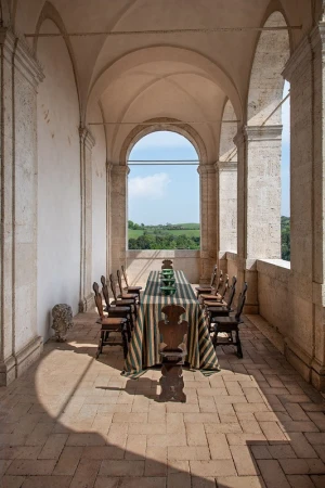 Stone archway frames an outdoor dining table set with striped tablecloth and green dishes, positioned on a stone patio with a rural view.