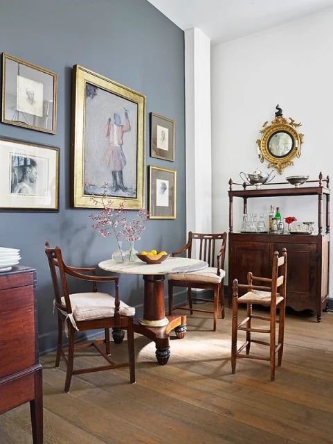 Traditional dining room interior with a round table, wooden chairs, and vintage art on a grey wall creating a classic, elegant space.