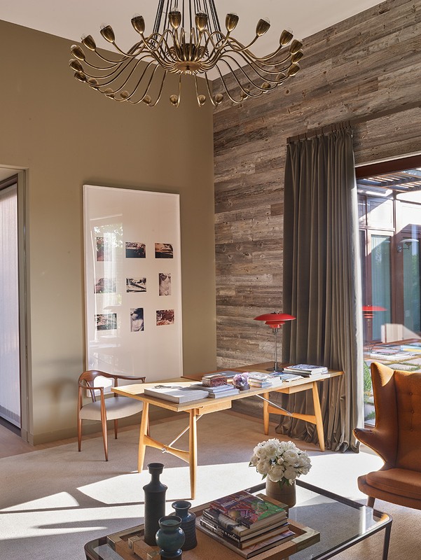 Living room interior featuring a light wood table with books, a glass coffee table with books and vases, and a unique chandelier.