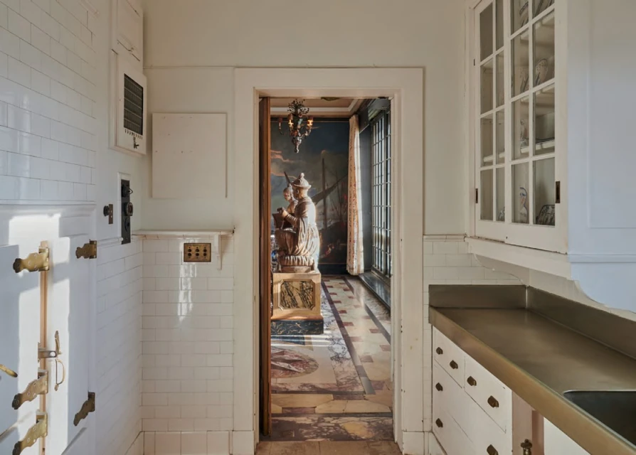 Interior view through a doorway showcases white tiled walls, a statue on a pedestal, and a mural in a well-lit room.