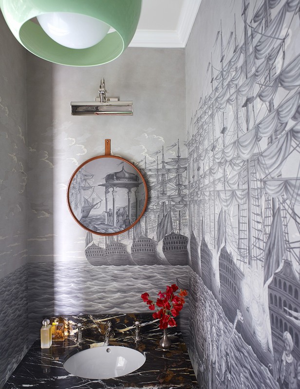 Interior view of a stylish powder room featuring black marble countertop, white sink, vintage-style ship wallpaper, and modern light fixture.