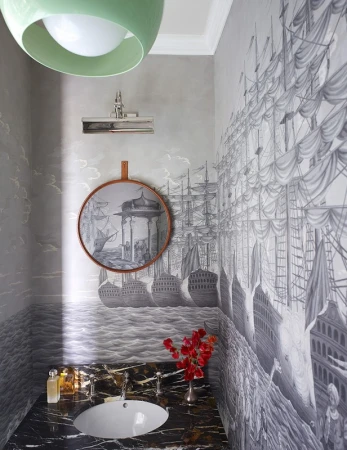 Interior view of a stylish powder room featuring black marble countertop, white sink, vintage-style ship wallpaper, and modern light fixture.