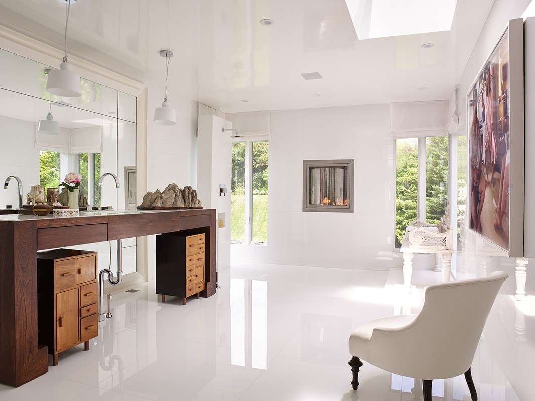 Bright bathroom interior with a dark wood vanity, white walls, light hardwood floors, a modern fireplace, and large picture on the wall.