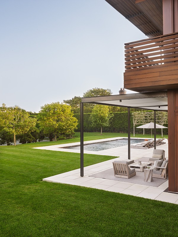 Exterior view of a modern house with a swimming pool, outdoor seating, a manicured lawn, and mature trees creating a serene backyard space.