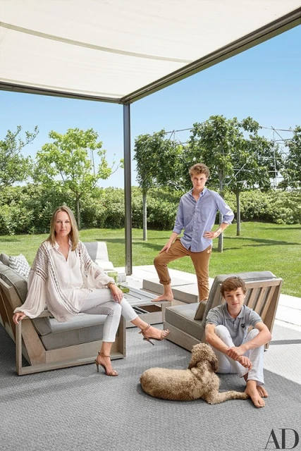 Family portrait on a patio features a woman, two boys, and a dog, with outdoor furniture and a lawn in the background on a sunny day.
