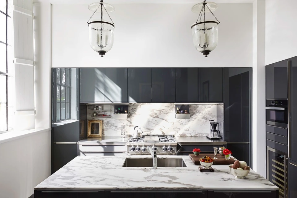 Contemporary kitchen interior featuring a marble island, grey cabinets, modern appliances, and elegant glass pendant lights.