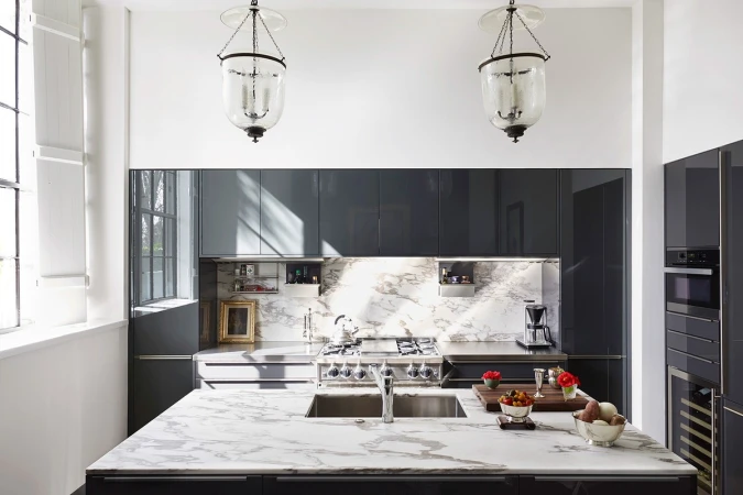 Contemporary kitchen interior featuring a marble island, grey cabinets, modern appliances, and elegant glass pendant lights.