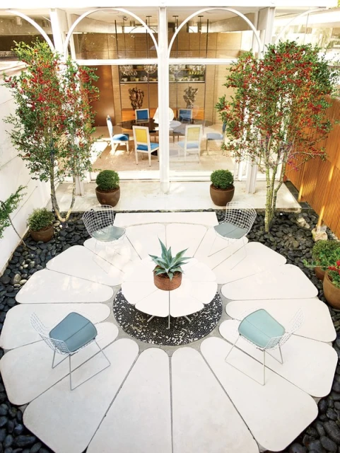 Outdoor patio area with a modern design, featuring a white table and chairs arranged in a unique flower-like pattern, surrounded by plants.