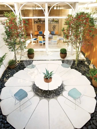 Outdoor patio area with a modern design, featuring a white table and chairs arranged in a unique flower-like pattern, surrounded by plants.