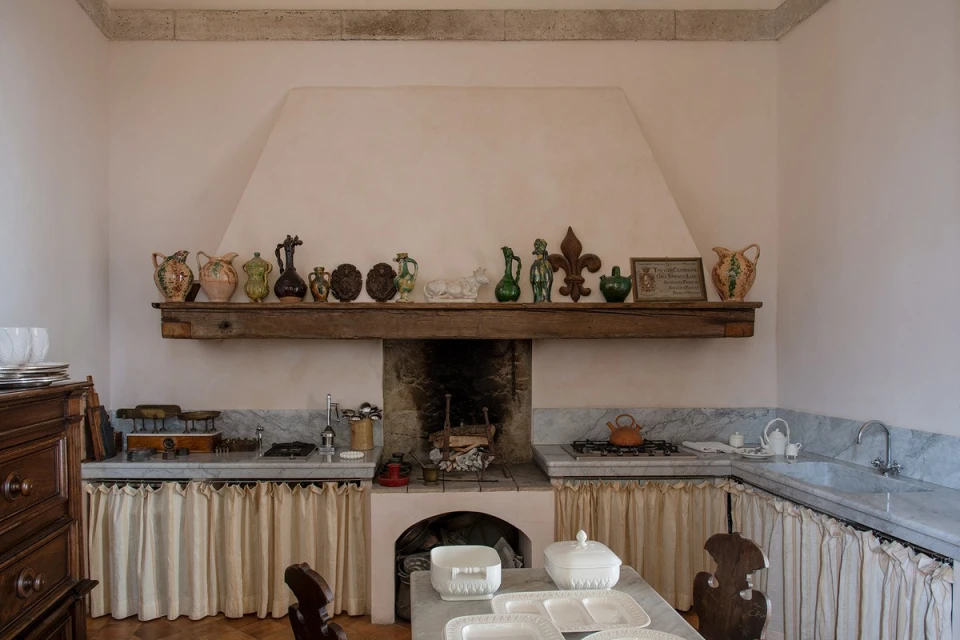 Traditional kitchen with marble countertops, wooden accents, open fireplace, decorative dishware, and light pink walls in a home interior.