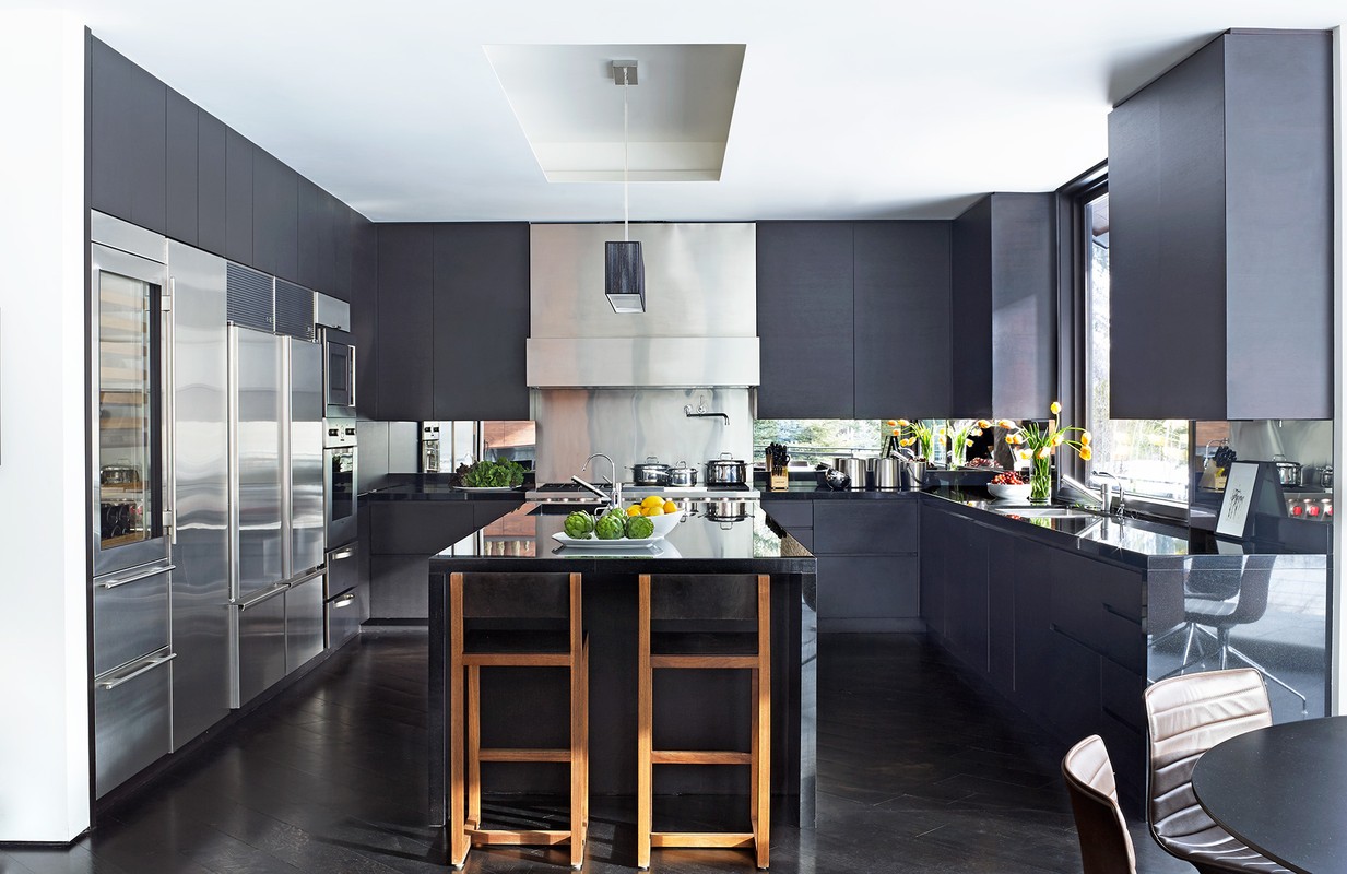 Contemporary kitchen interior featuring dark cabinets, stainless steel appliances, a central island with bar stools, and natural light.