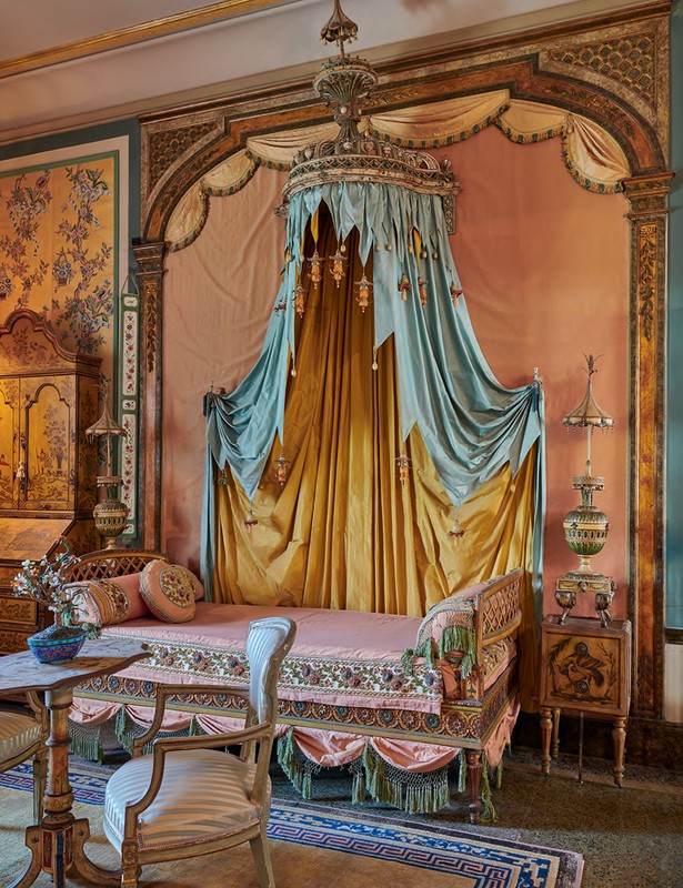Ornate interior with a daybed featuring a canopy, alongside decorative furniture and floral wallpaper in soft, muted colors and vintage style.