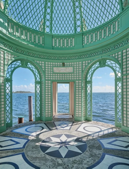 Ornate gazebo on a pier with geometric tile flooring, open to ocean view under a partly cloudy blue sky, providing architectural interest.