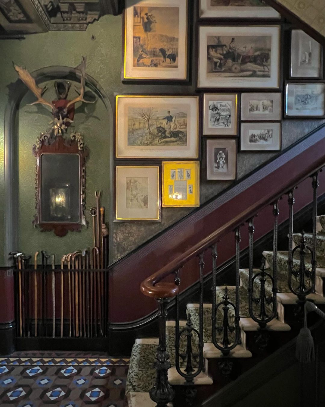 Grand interior staircase and ornate wall art. Elegant stair runner leads up to framed paintings and deer antler mount.