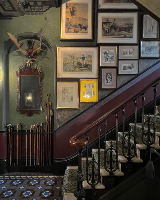 Grand interior staircase and ornate wall art. Elegant stair runner leads up to framed paintings and deer antler mount.