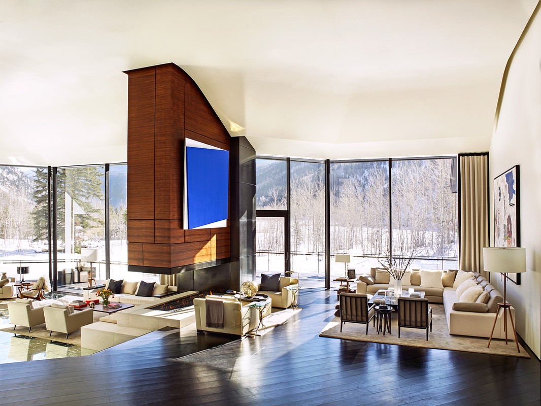 Bright living room with large windows framing a snowy mountain view, comfortable furniture, and a modern fireplace with a large blue painting.