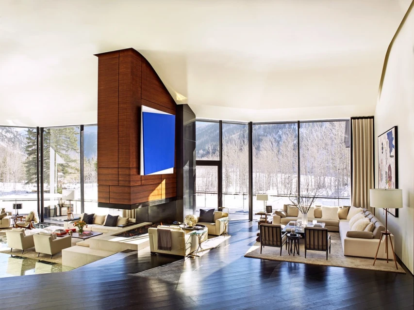 Bright living room with large windows framing a snowy mountain view, comfortable furniture, and a modern fireplace with a large blue painting.