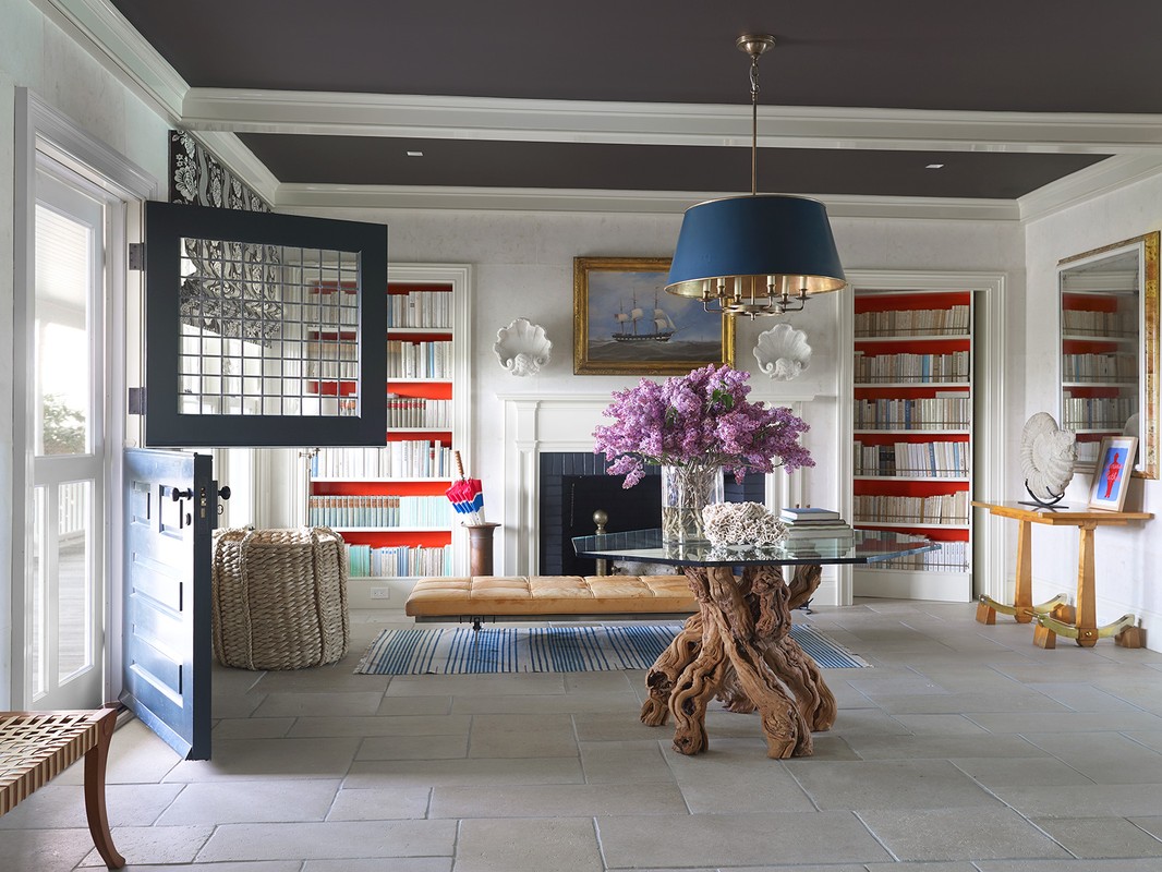 Interior view of a home entryway featuring a driftwood table with flowers, a dutch door, and built-in bookshelves in a bright, stylish space.
